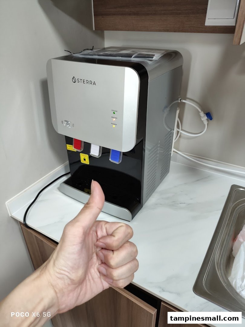 A Sterra water dispenser on a counter with a hand giving a thumbs-up.