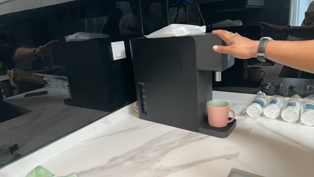 A person operates a sleek black water dispenser on a modern counter, with new filters visible.