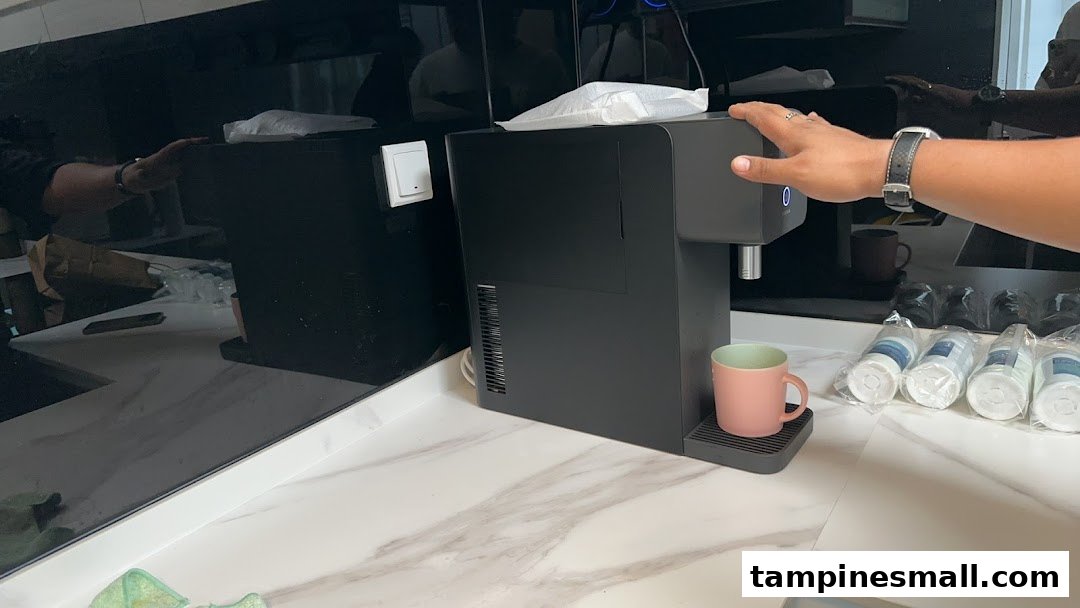 A person operates a sleek black water dispenser on a modern counter, with new filters visible.