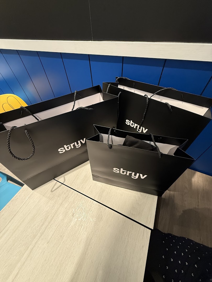 Several black Stryv shopping bags with white logos are placed on a light wooden surface.