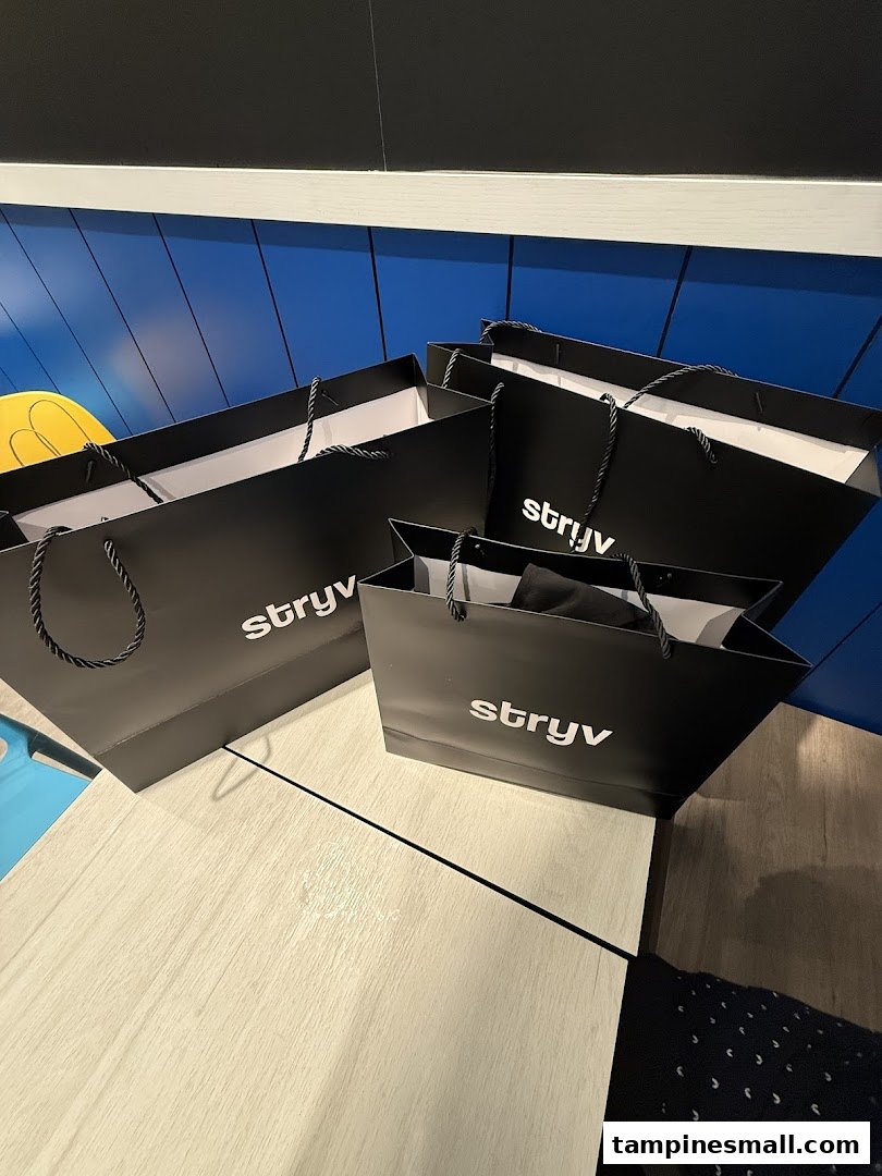 Several black Stryv shopping bags with white logos are placed on a light wooden surface.