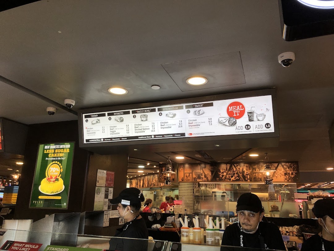 Digital menu board at Stuffd showcasing kebabs, burritos, bowls, and tacos with staff preparing orders.