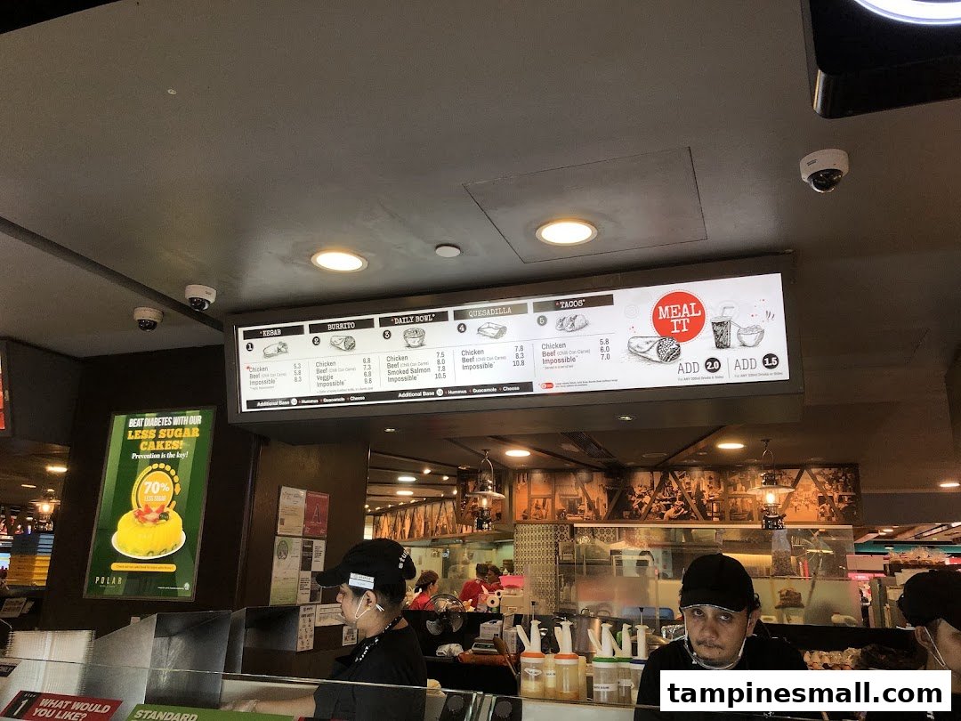 Digital menu board at Stuffd showcasing kebabs, burritos, bowls, and tacos with staff preparing orders.