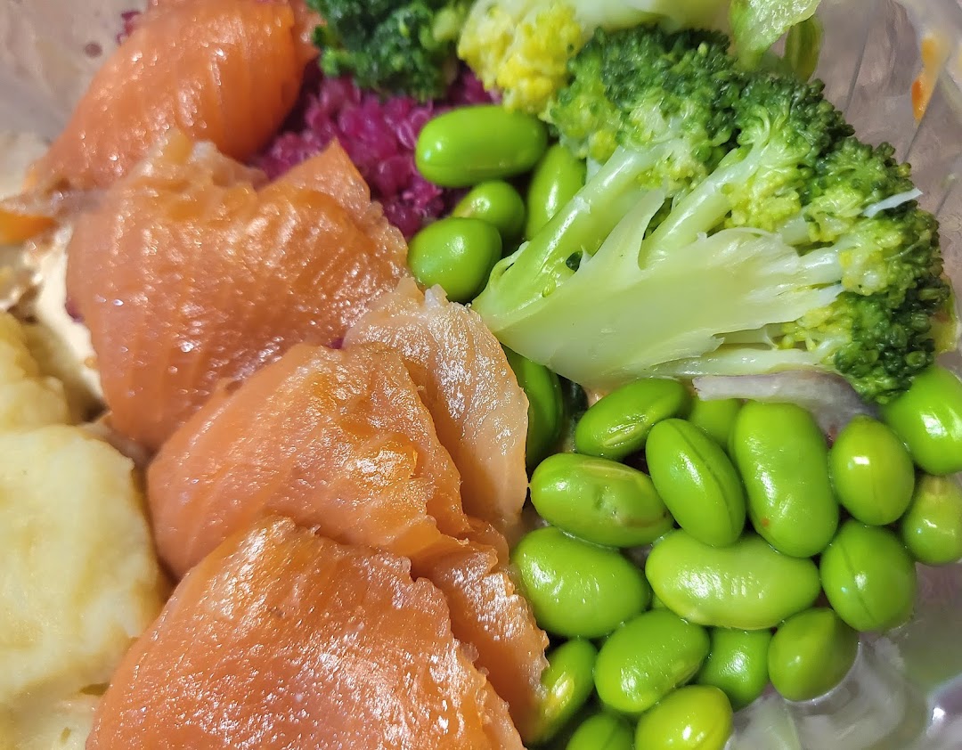 A vibrant close-up of a healthy meal bowl featuring salmon, edamame, broccoli, and a creamy base.