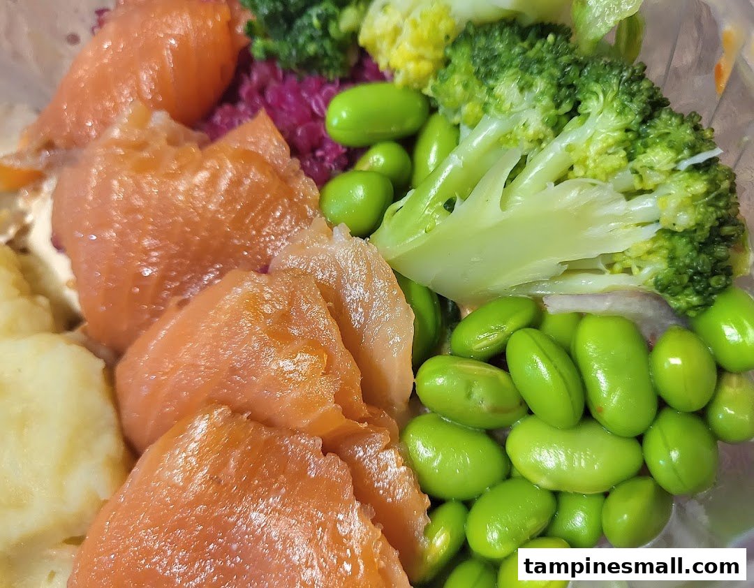 A vibrant close-up of a healthy meal bowl featuring salmon, edamame, broccoli, and a creamy base.