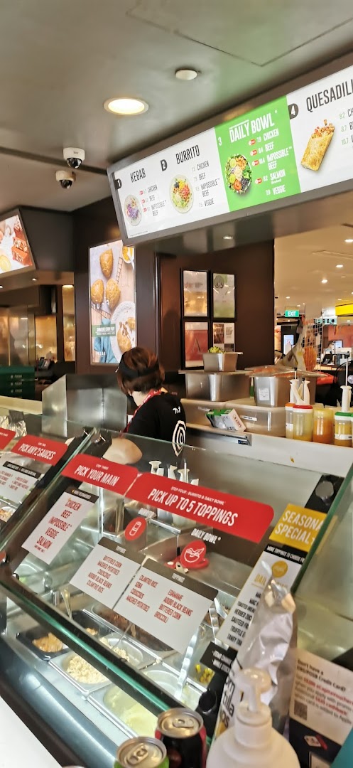 A staff member prepares customizable meals at Stuffd, featuring digital menu boards and fresh ingredients.