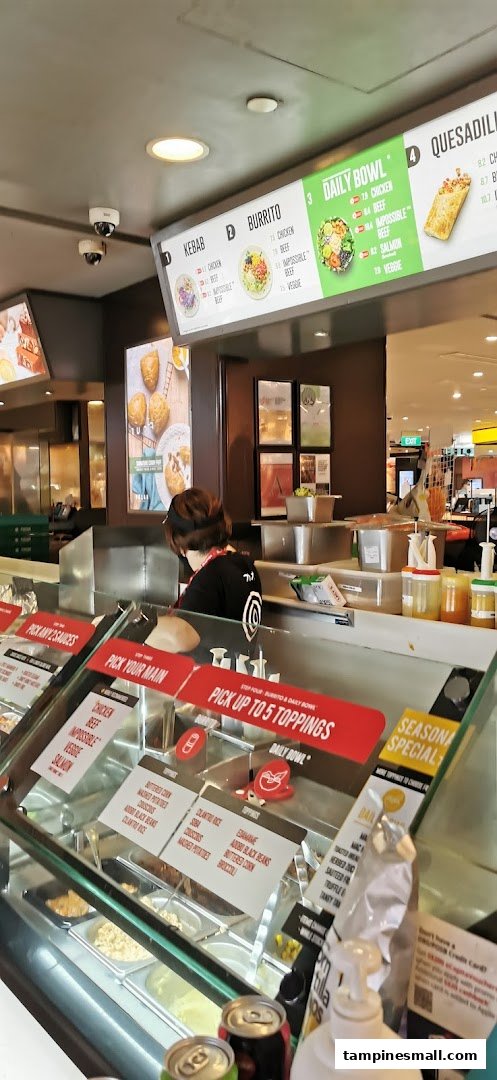 A staff member prepares customizable meals at Stuffd, featuring digital menu boards and fresh ingredients.