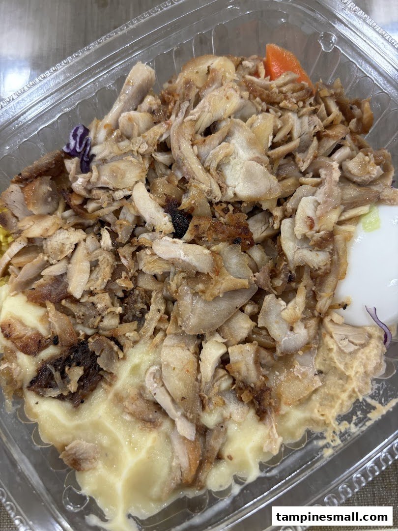 A close-up of a Stuffd chicken bowl with shredded meat over a creamy base in a clear container.