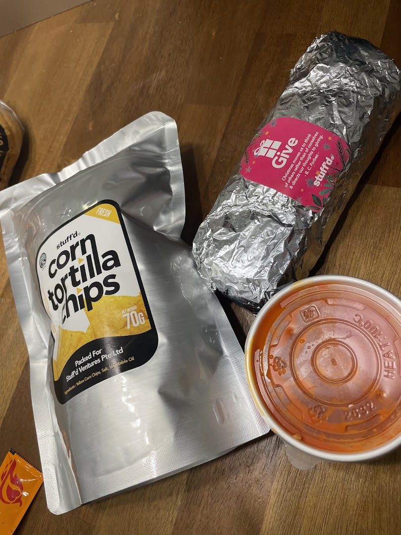 A Stuffd burrito, corn tortilla chips, and a dip are displayed on a wooden surface.