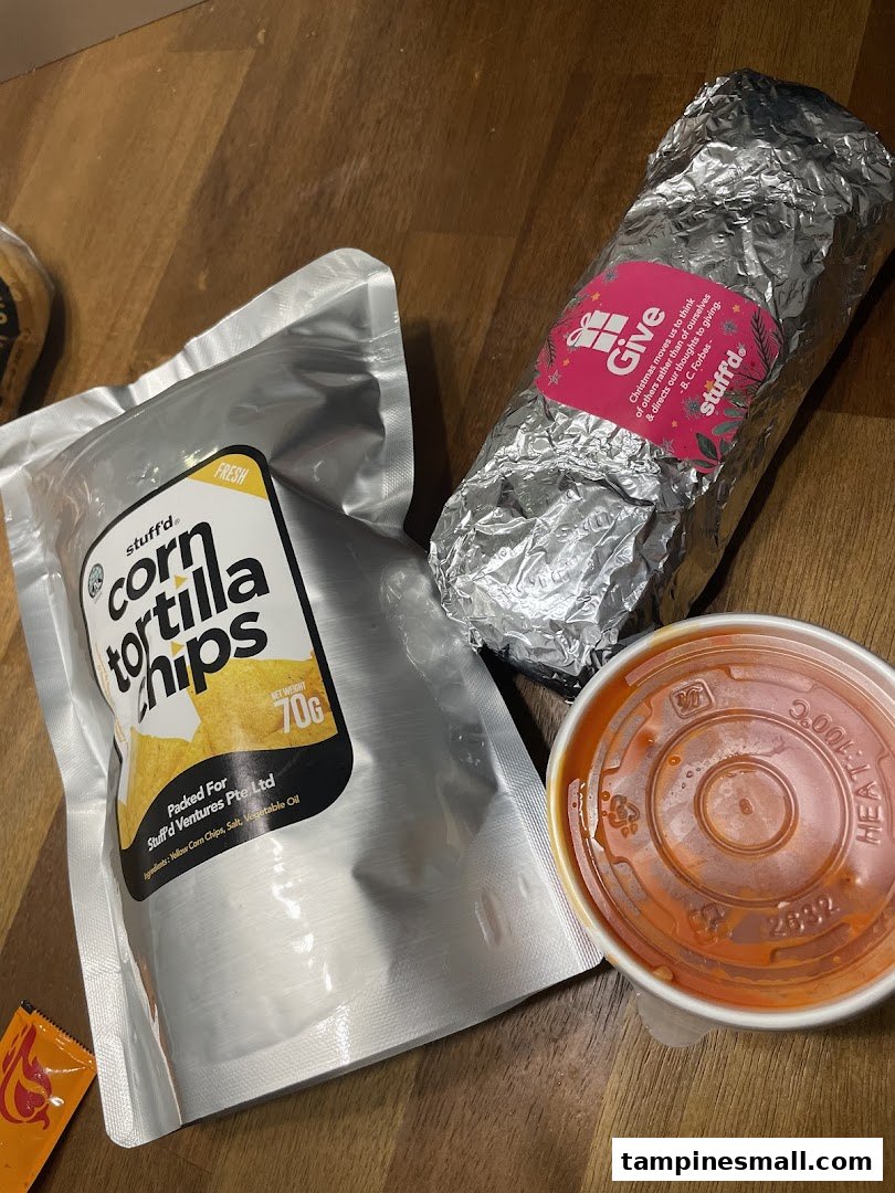A Stuffd burrito, corn tortilla chips, and a dip are displayed on a wooden surface.