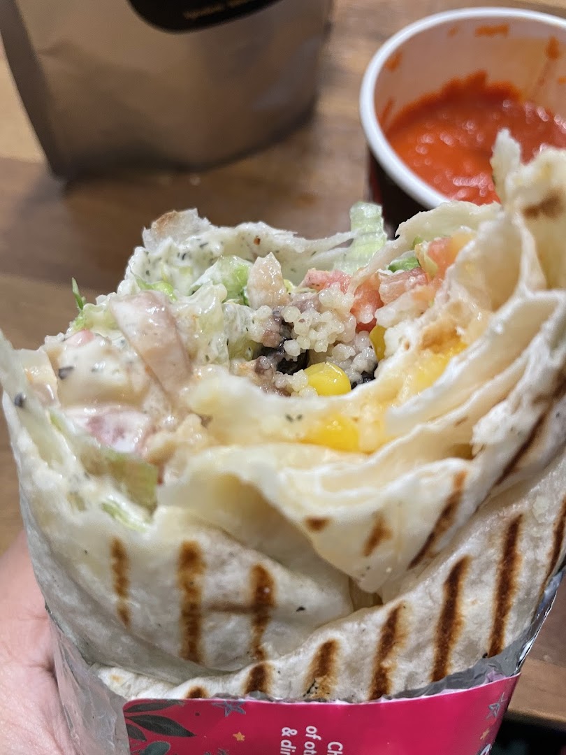 A close-up of a delicious, freshly made wrap filled with various ingredients, served with a side of red sauce.
