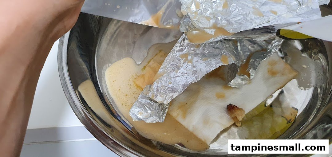 A metal bowl containing food remnants, liquid, and crumpled aluminum foil after a meal.