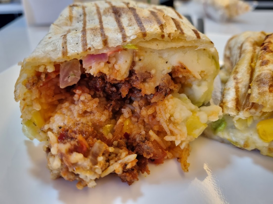 A close-up of a grilled wrap, cut open to reveal a hearty filling of rice, meat, potatoes, and vegetables.