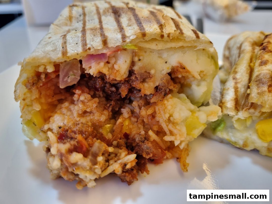 A close-up of a grilled wrap, cut open to reveal a hearty filling of rice, meat, potatoes, and vegetables.
