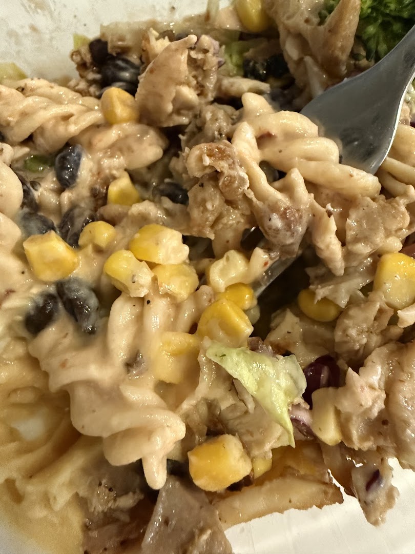 A close-up of a creamy pasta dish with chicken, corn, and black beans, being served with a fork.