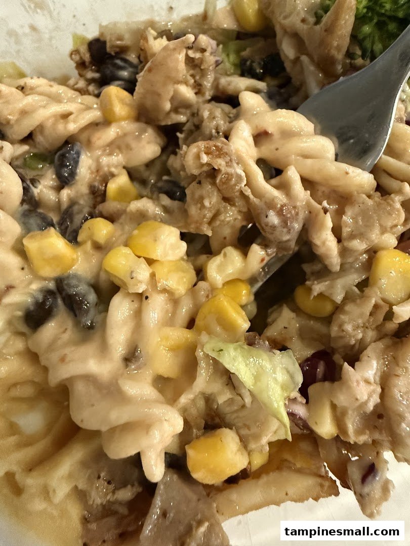 A close-up of a creamy pasta dish with chicken, corn, and black beans, being served with a fork.