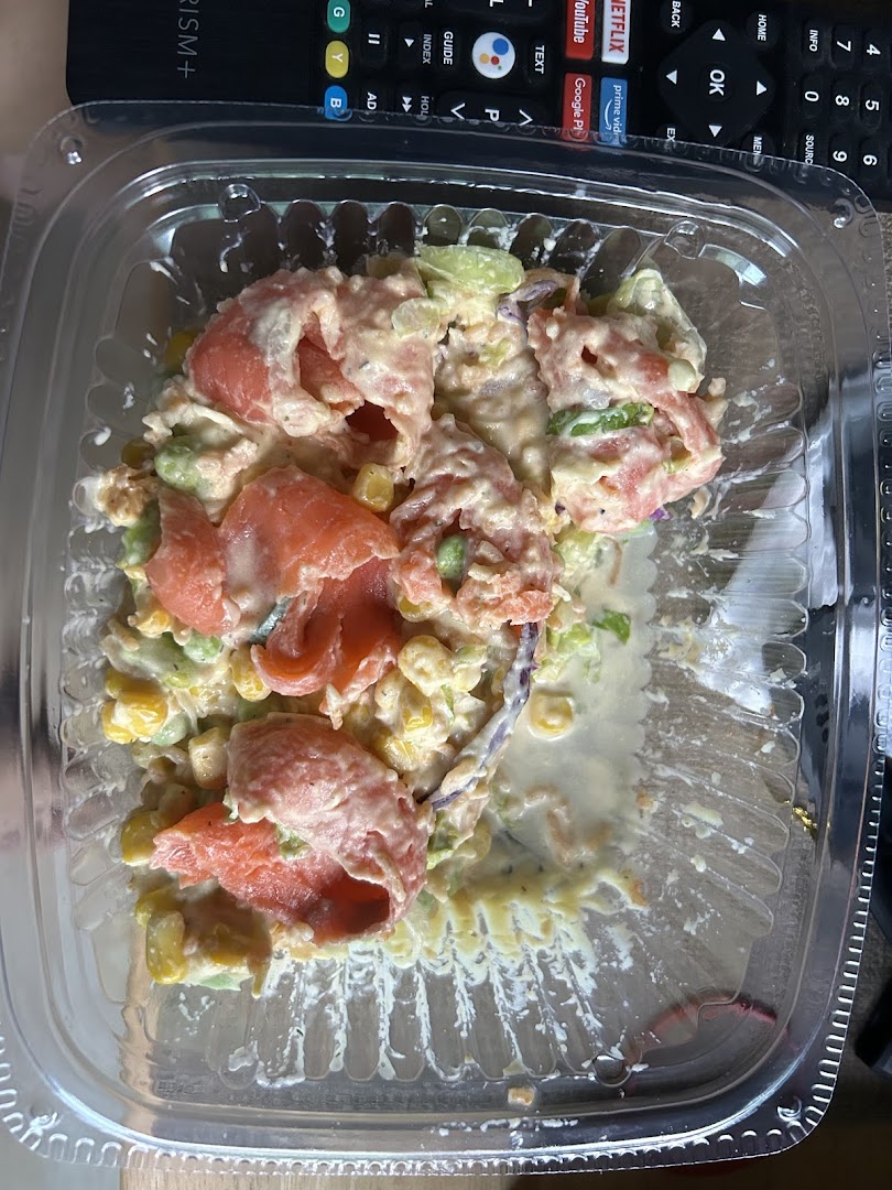A close-up of a fresh salad or bowl with salmon, corn, and a creamy dressing in a clear plastic container.