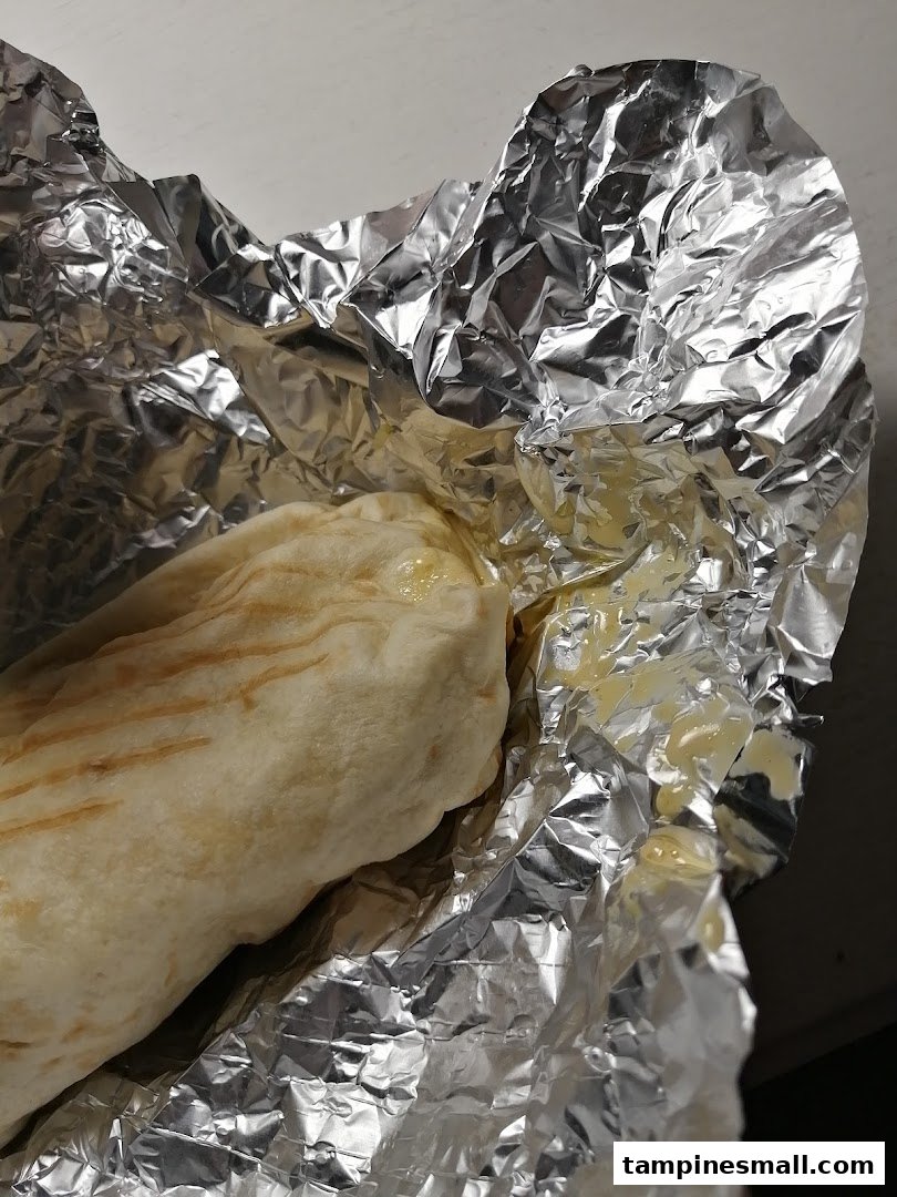 A close-up of a delicious wrap or burrito, partially unwrapped from its foil packaging.