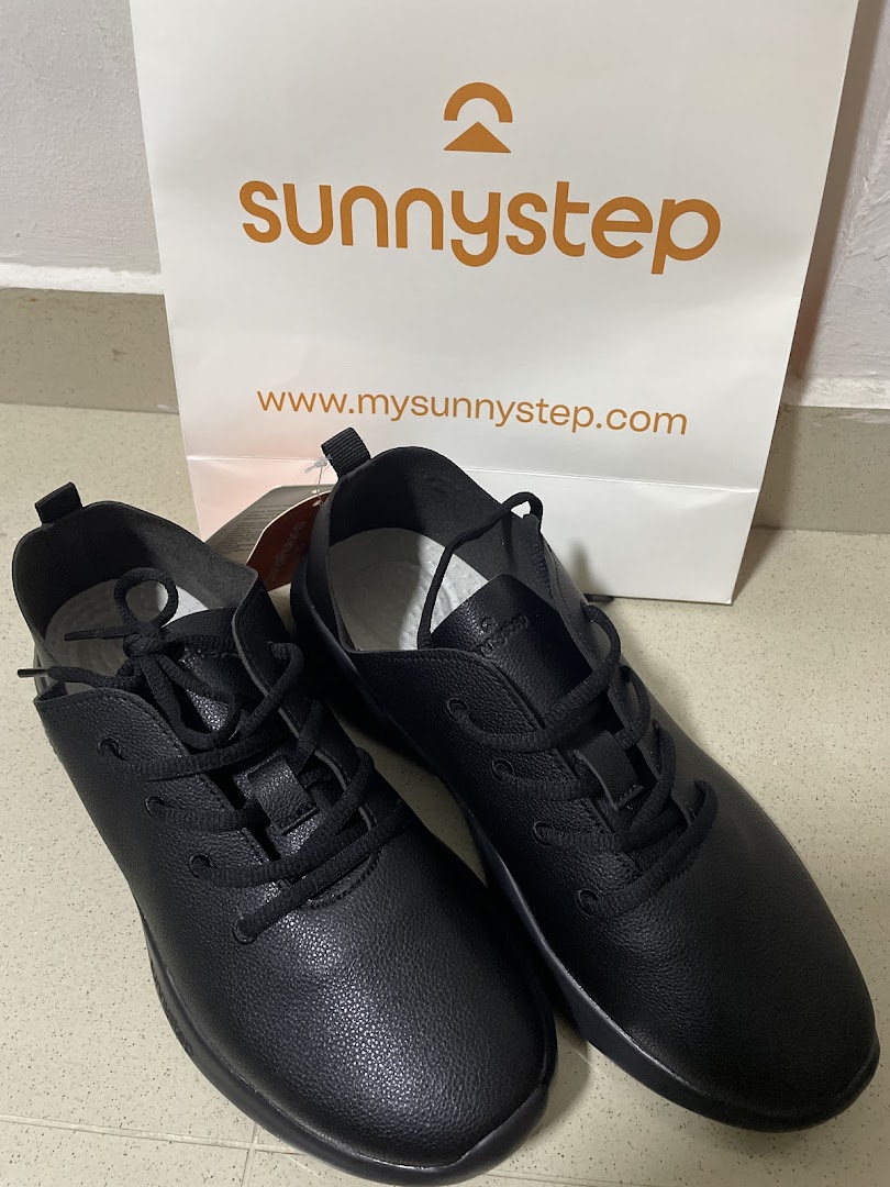 A pair of black Sunnystep shoes next to a branded shopping bag.