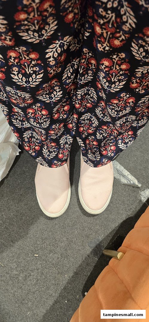 A person wearing patterned pants and light pink slip-on shoes stands on a grey carpet.