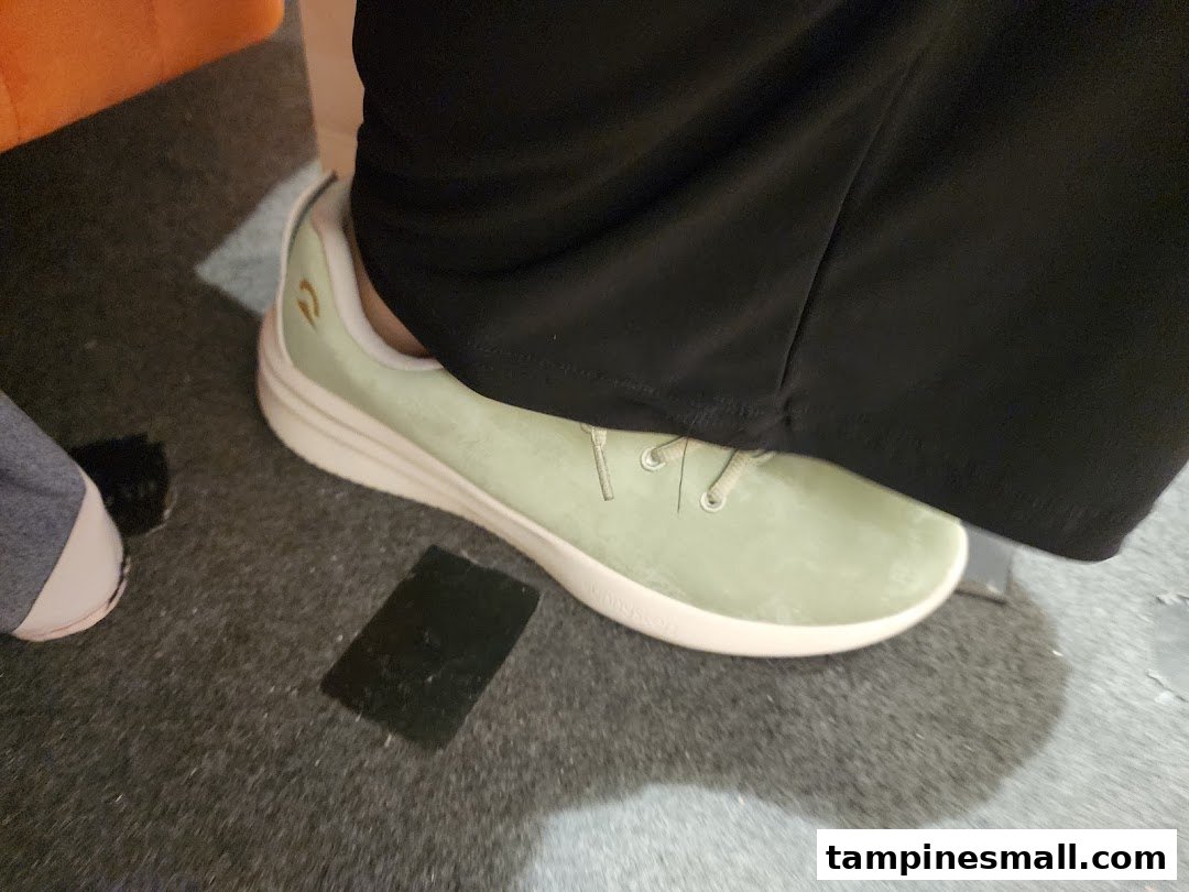 A close-up of a person's foot wearing a light green Sunnystep shoe on a dark carpeted floor.