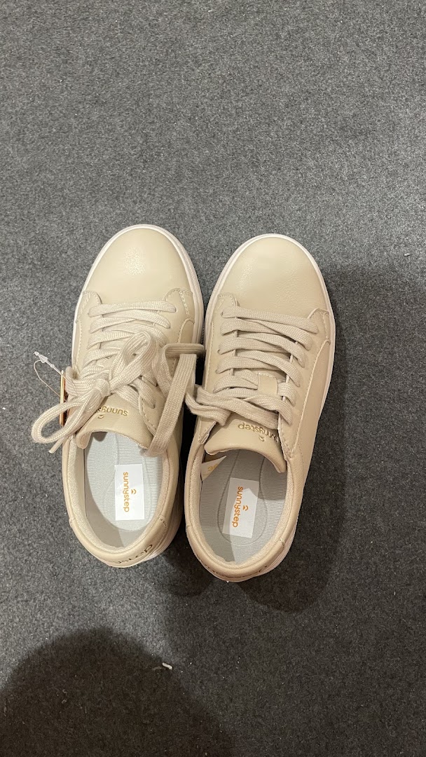 A pair of new beige Sunnystep sneakers with tags on a dark grey floor.