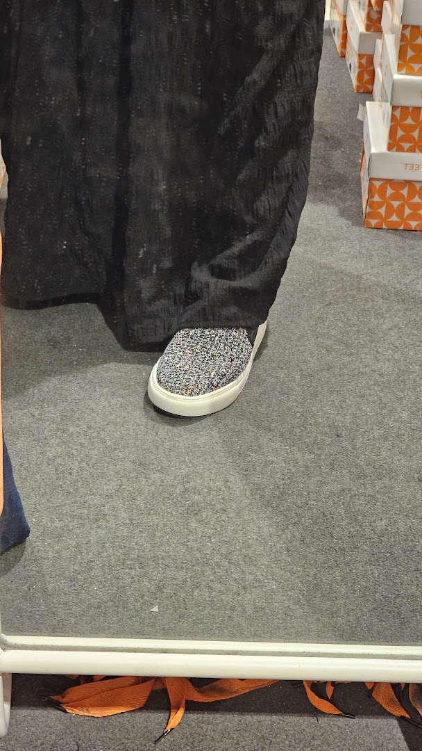 A person's foot wearing a sparkly slip-on shoe, reflected in a mirror, inside a footwear store.