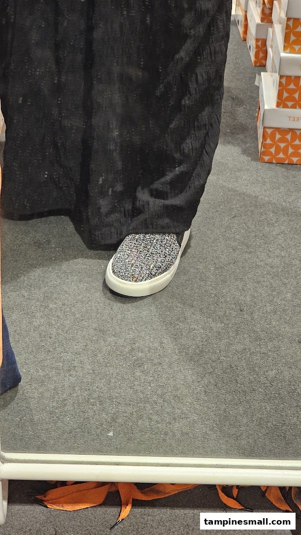 A person's foot wearing a sparkly slip-on shoe, reflected in a mirror, inside a footwear store.