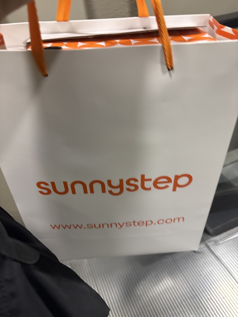 A white Sunnystep shopping bag with orange handles and logo, featuring their website address.
