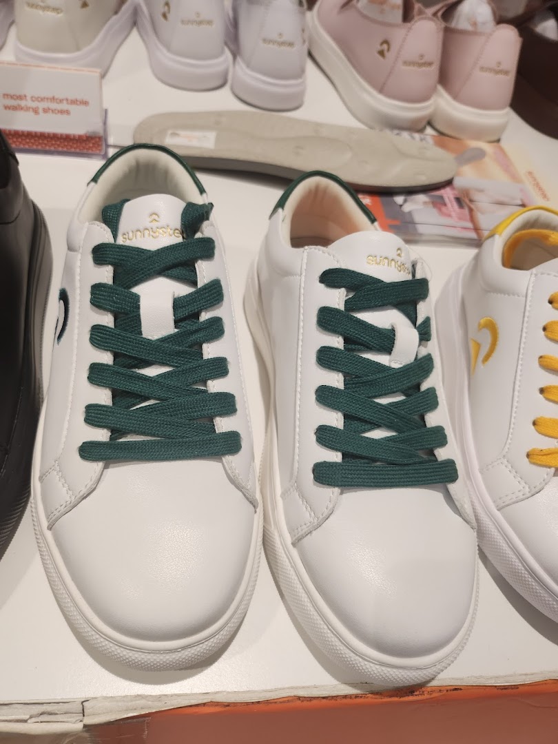 Close-up of white Sunnystep sneakers with dark green laces on display.