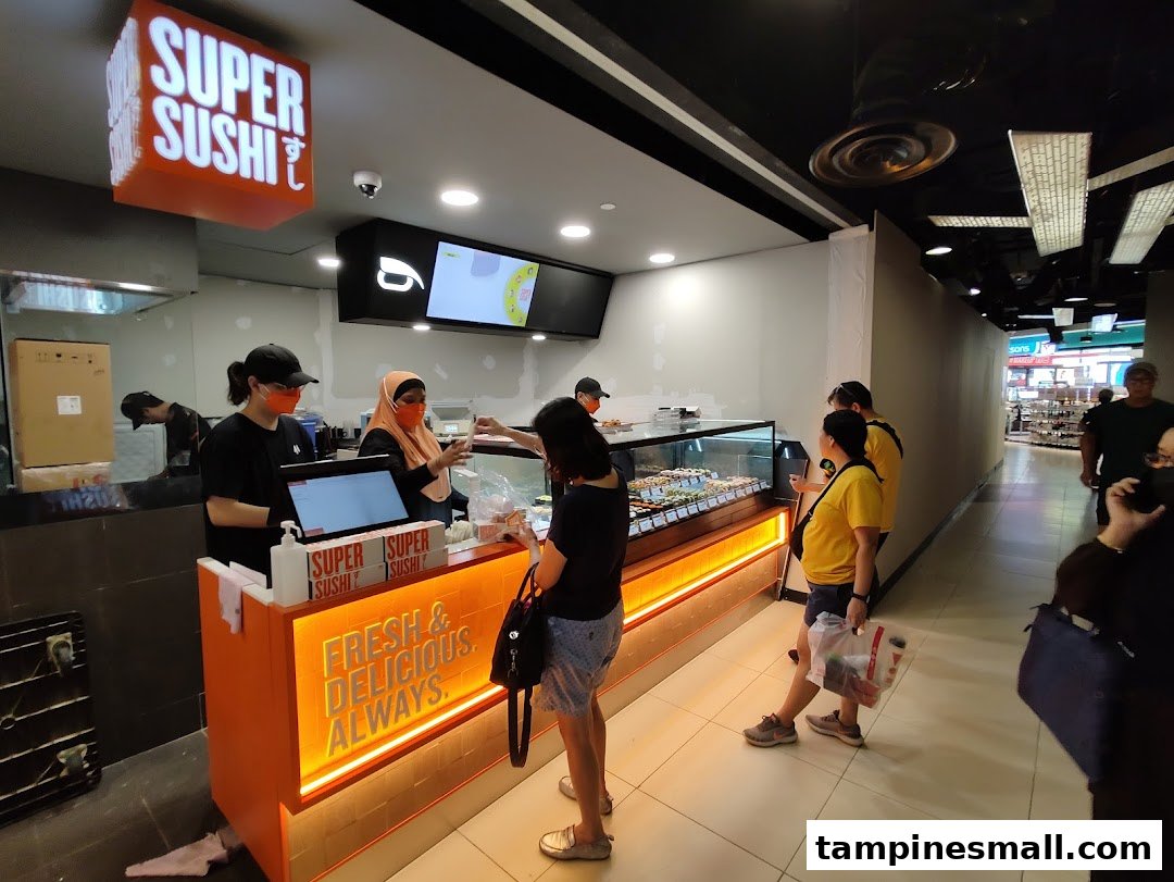Customers interact with staff at the Super Sushi counter, featuring a display of fresh sushi and a 'Fresh & Delicious. Always.' sign.