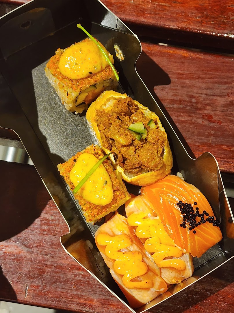 A close-up of a variety of gourmet sushi and Japanese dishes in a takeaway box.