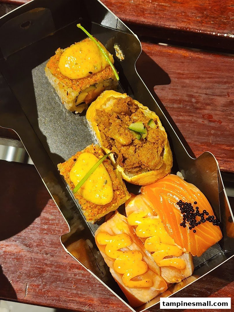 A close-up of a variety of gourmet sushi and Japanese dishes in a takeaway box.