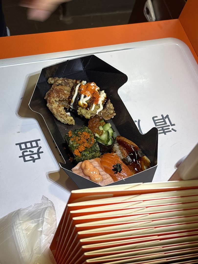 A black takeout box filled with assorted sushi, nigiri, and fried chicken, ready to enjoy.