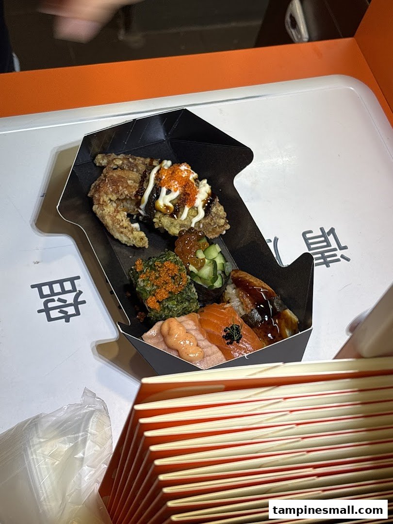 A black takeout box filled with assorted sushi, nigiri, and fried chicken, ready to enjoy.