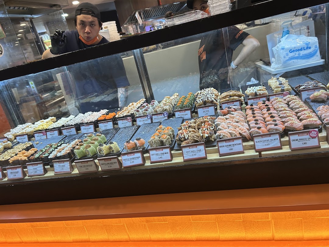 A vibrant display of fresh sushi and maki rolls with staff preparing orders at Super Sushi.