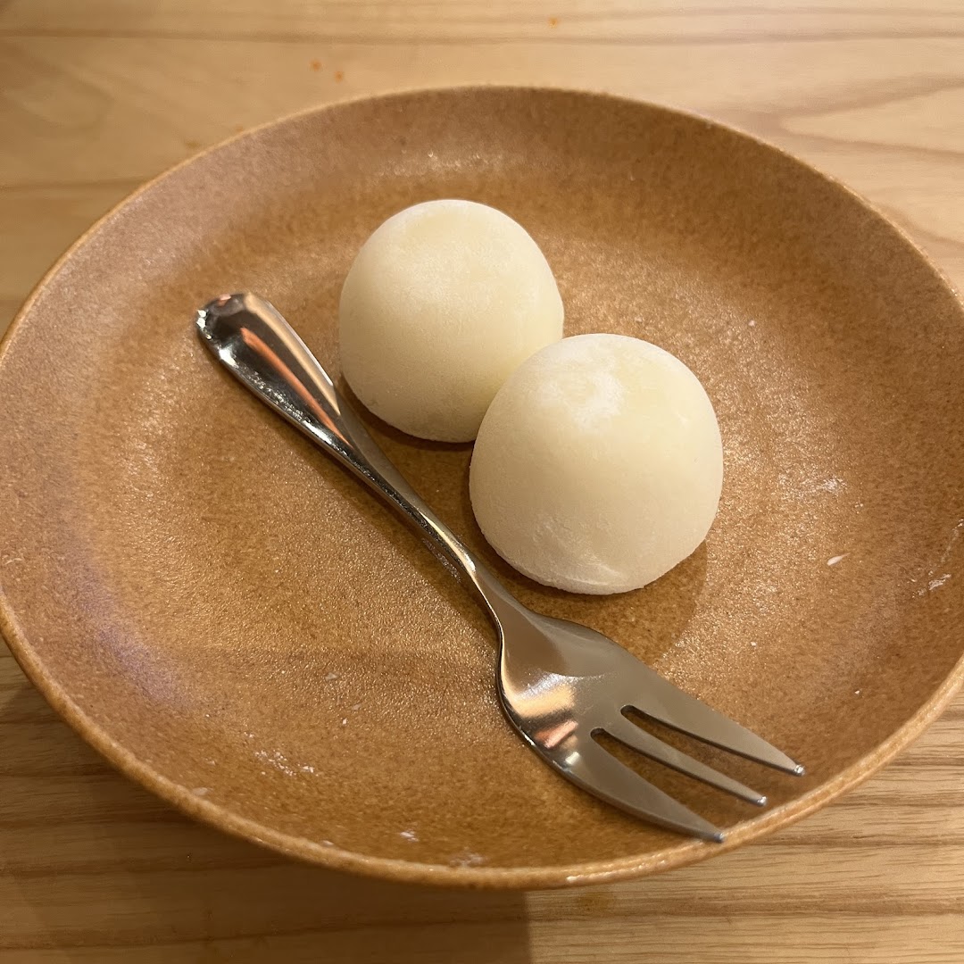 Two white mochi desserts on a brown plate with a fork, ready to be enjoyed.