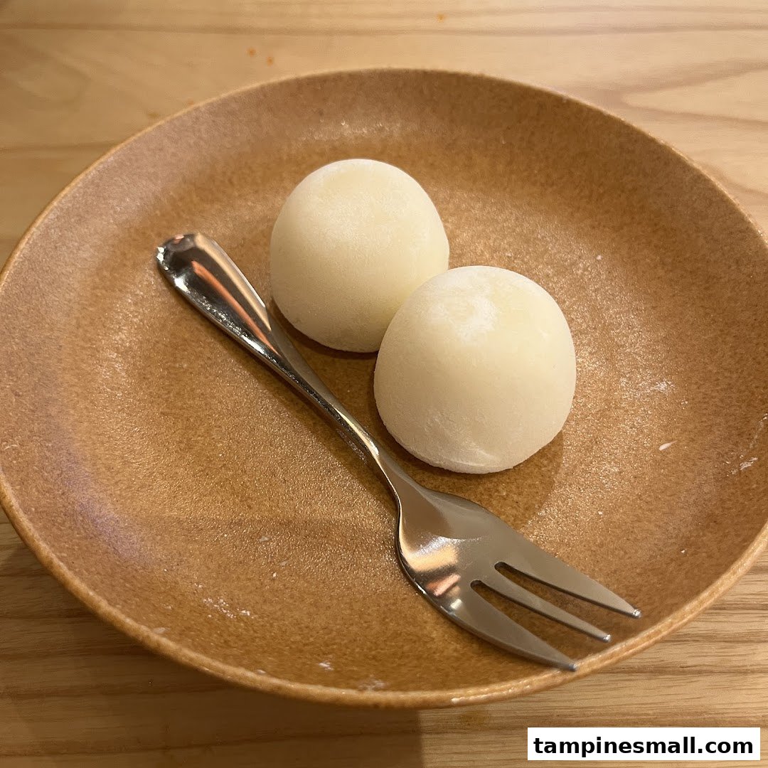 Two white mochi desserts on a brown plate with a fork, ready to be enjoyed.