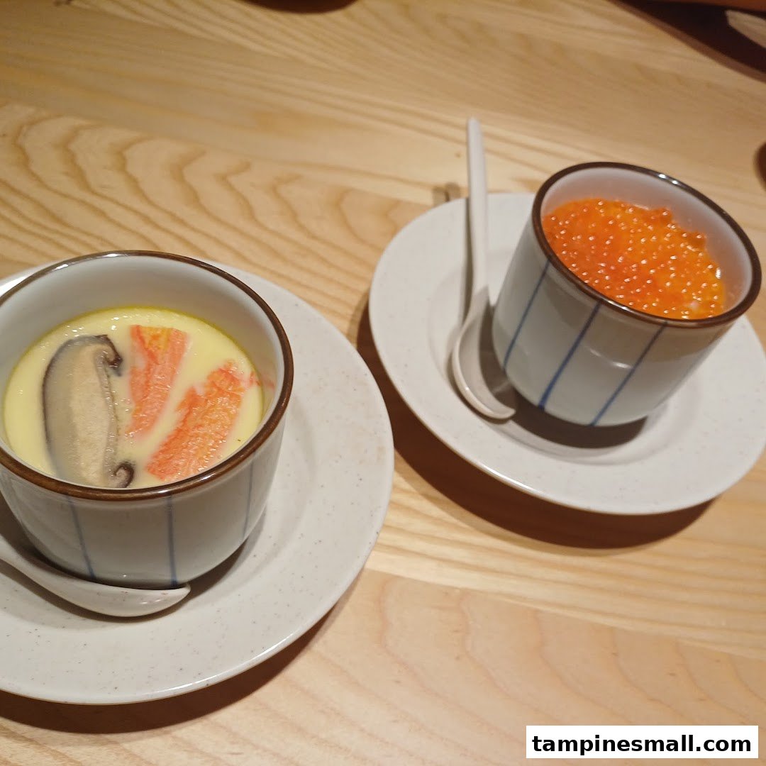 Two Japanese dishes, chawanmushi and ikura, served in traditional cups on a wooden table.