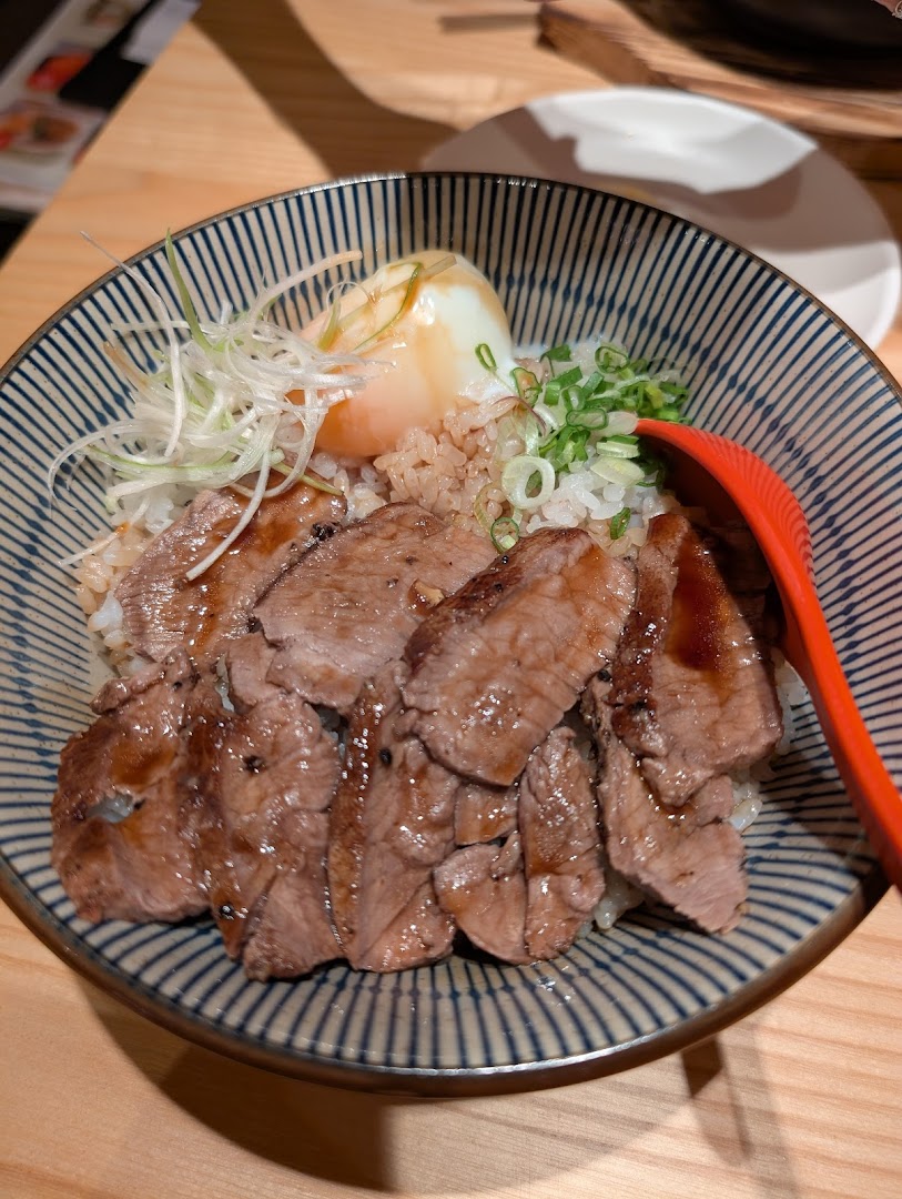 A delicious bowl of sliced meat over rice with a poached egg and green onions.
