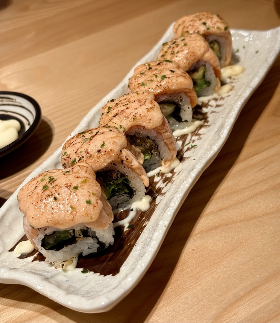 A plate of torched salmon sushi rolls with a creamy sauce and herbs on a white platter.