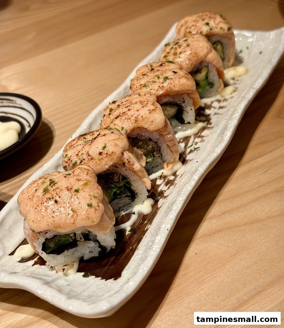 A plate of torched salmon sushi rolls with a creamy sauce and herbs on a white platter.
