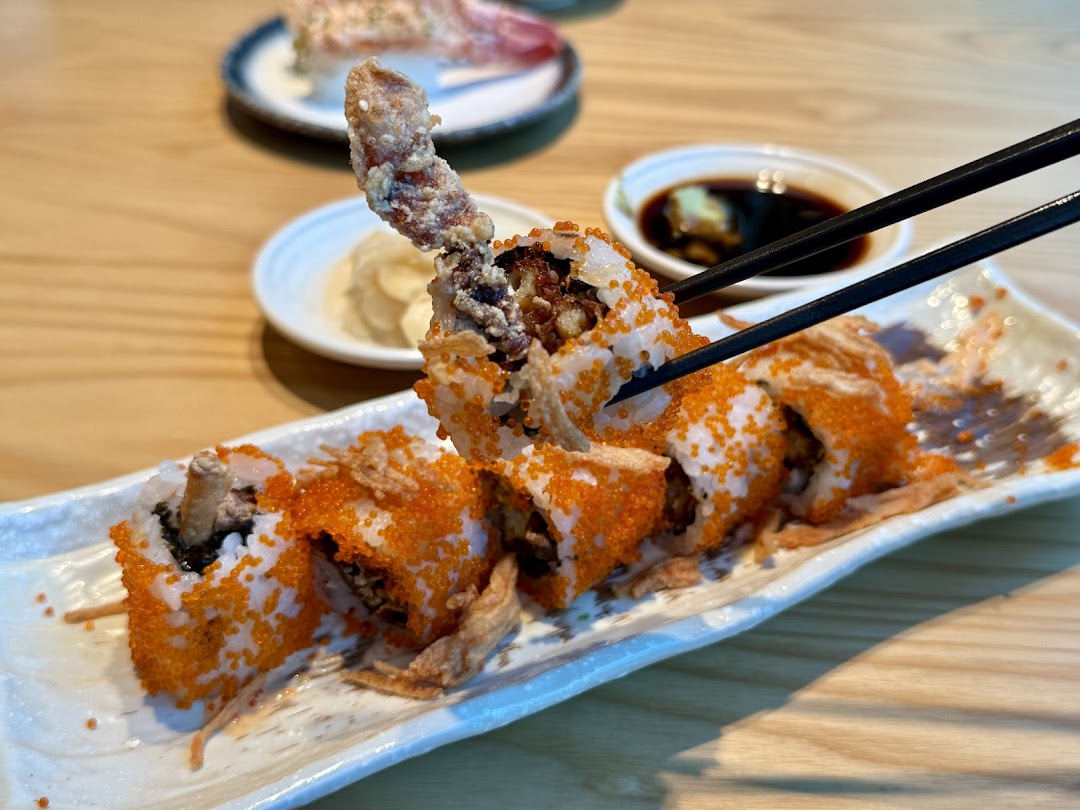 Chopsticks picking up a piece of crispy soft-shell crab maki sushi with vibrant flying fish roe.
