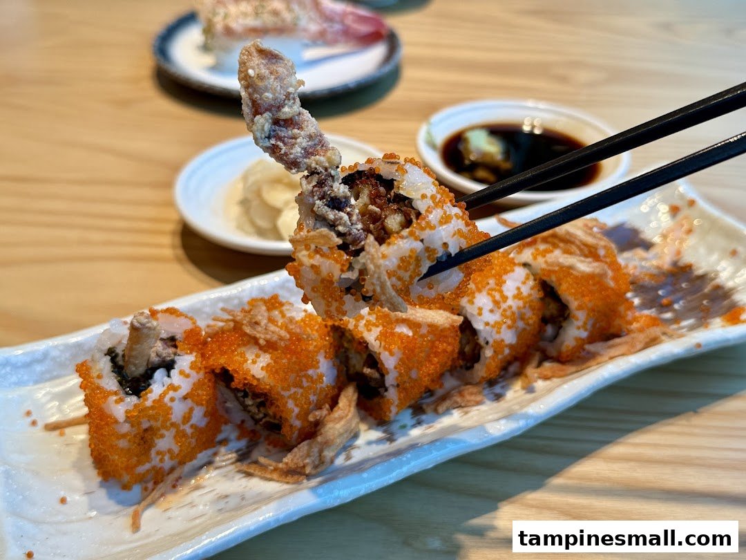Chopsticks picking up a piece of crispy soft-shell crab maki sushi with vibrant flying fish roe.