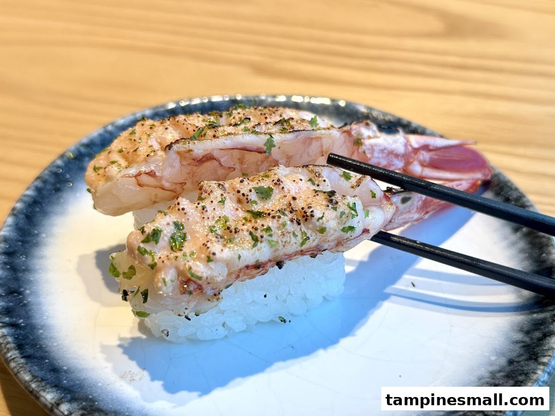 Two pieces of flame-seared shrimp sushi (aburi ebi nigiri) on a plate with chopsticks.