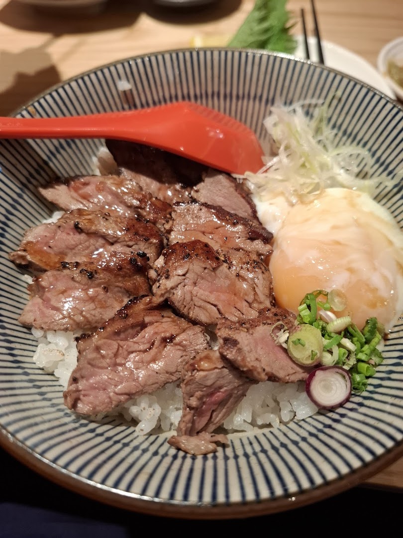 A delicious bowl of grilled beef slices with rice, a poached egg, and fresh garnishes.