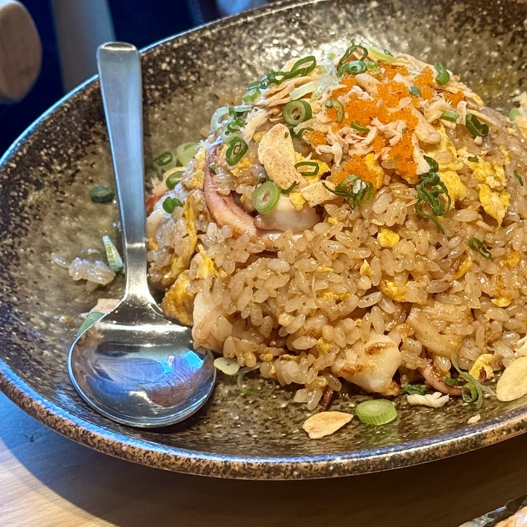 A close-up of delicious seafood fried rice topped with tobiko, green onions, and crispy garlic.