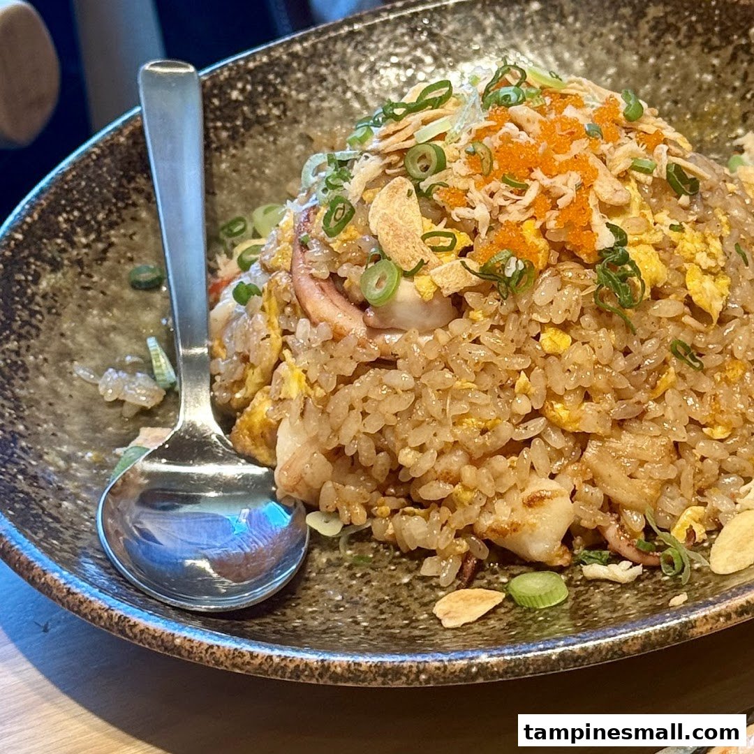 A close-up of delicious seafood fried rice topped with tobiko, green onions, and crispy garlic.