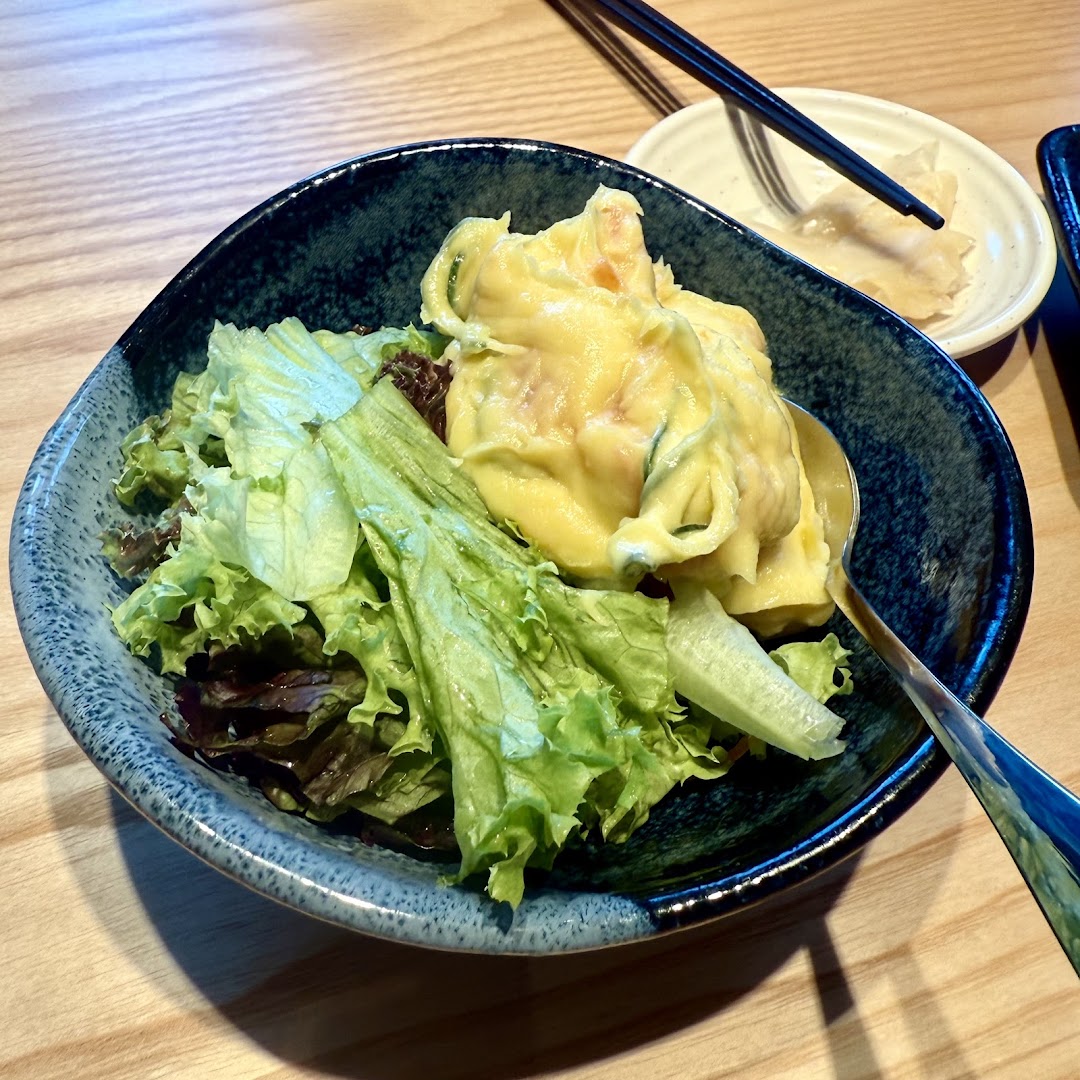 A fresh salad with creamy potato salad served in a dark blue bowl on a wooden table.