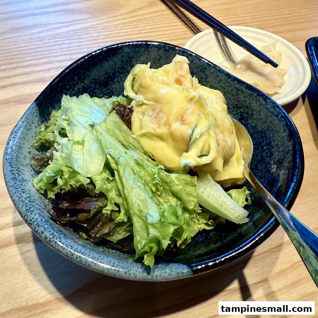 A fresh salad with creamy potato salad served in a dark blue bowl on a wooden table.